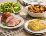 Un rôti de porc tranché, servi avec une salade verte, des légumes rôtis et un gratin dauphinois. Parfait accompagnement froid pour viande.