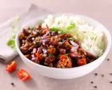 Un bol de riz blanc et de chili con carne recette de chef, garni d'oignons rouges et de persil. Des tomates cerises et du poivre en grains décorent la table.