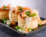 Trois bouchées de tapas crevette, garnies de crevettes, petits pois et sauce crémeuse, sur un plateau noir.