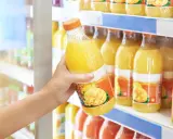 Une main choisit une bouteille de ce qui semble être le meilleur jus de fruit, avec des mangues et des ananas sur l'étiquette.