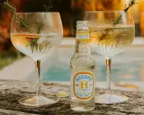 Une bouteille de tonic Hysopé Original, prête à être versée dans deux verres de gin rafraîchissants, décorés de romarin et d'une tranche d'orange.