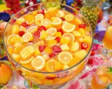 Un grand bol de punch aux fruits colorés, parfait pour une recette de punch sans alcool pour 30 personnes. Fraises, oranges, citrons et morceaux de pêche flottent dans un liquide orangé.