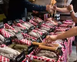 Vitrine de charcuterie avec de nombreuses saucisses et un client qui en choisit une tranche.