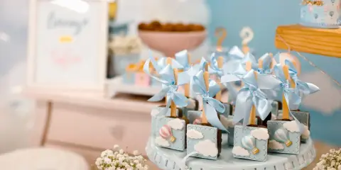 Garniture de table pour baby shower avec des chocolats décorés de montgolfières bleues et de nuages.