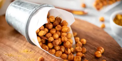 Un seau renversé déverse des pois chiches rôtis, parfaits pour des snacks sains. Une pincée d'épices dorées parsème le bois.