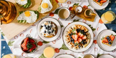Un petit déjeuner continental ou américain avec des toasts à l'avocat et aux œufs, des gaufres aux fruits rouges et des jus.