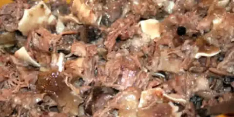 Un plat de fromage de tête, avec des morceaux de viande et de cartilage, dans un récipient en bois.