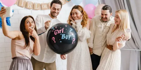 Groupe d'amis joyeux lors d'une annonce sexe du bébé. Un ballon noir avec "Girl? Boy?" au centre de la scène.