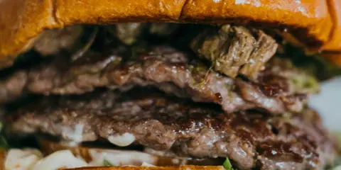 Gros plan sur un steak burger double, avec des steaks juteux, de la sauce et de la laitue entre deux pains briochés dorés.