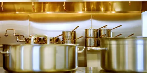 Une cuisine professionnelle avec des casseroles en acier inox 18/10 étincelantes. Des robinets chromés et des gicleurs de sécurité complètent l'ensemble.