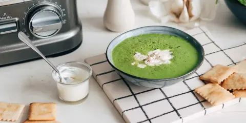 Une délicieuse soupe de légumes variés, onctueuse et verte, garnie de crème et servie avec des crackers.