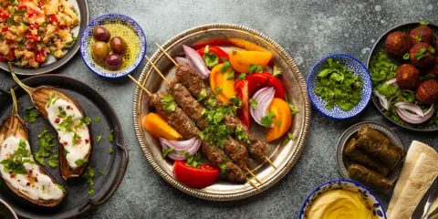 Un festin de plat méditerranéen : brochettes de viande, aubergines rôties, falafels, feuilles de vigne farcies, houmous et salade de couscous.