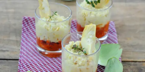 Trois verrines artichaut, garnies d'une purée crémeuse et d'une touche de sauce tomate, sur un fond de bois rustique.