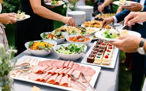 Un buffet garni pour un plat soiree : salades fraîches, charcuteries, et petits gâteaux décorés. Les invités se servent.