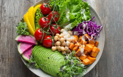Un bol coloré avec avocat, tomates, pois chiches, patates douces, chou rouge, radis et poivron jaune. Parfaites salades originales pour buffet.