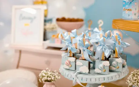 Garniture de table pour baby shower avec des chocolats décorés de montgolfières bleues et de nuages.