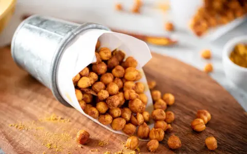 Un seau renversé déverse des pois chiches rôtis, parfaits pour des snacks sains. Une pincée d'épices dorées parsème le bois.