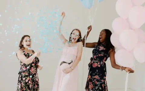 Trois femmes célèbrent un gender reveal, avec des confettis bleus et des ballons roses et bleus. C'est quoi ce moment joyeux !