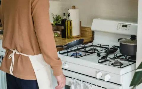 Un homme en tablier prépare à nettoyer graisse brûlée gazinière. Une poêle chauffe sur le feu.