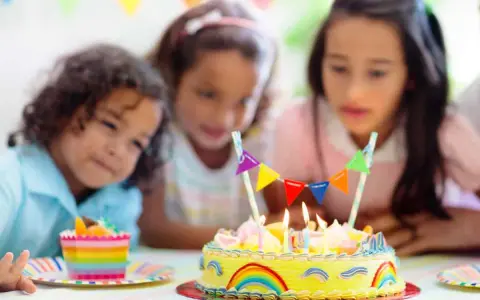 Trois enfants regardent un gâteau d'anniversaire jaune décoré d'arcs-en-ciel et de fanions. Le meilleur goût gâteau anniversaire est prêt à être dégusté.