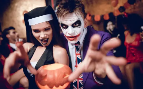 Un couple en costumes effrayants, une nonne et le Joker, profite d'une **soirée costumée** d'Halloween, tenant une citrouille sculptée.