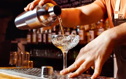Un barman verse un liquide d'un shaker dans un verre à cocktail rempli de glace. Les shakers sont essentiels pour créer des boissons rafraîchissantes.