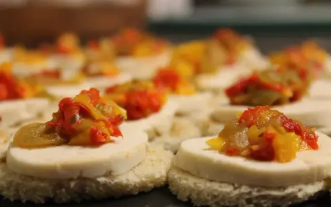 Petits toasts pour l'apéro, garnis de fromage blanc et d'une préparation colorée de poivrons et oignons.