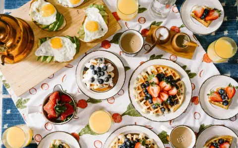 Un petit déjeuner continental ou américain avec des toasts à l'avocat et aux œufs, des gaufres aux fruits rouges et des jus.