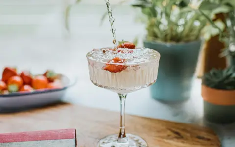 Un cocktail sans alcool surprenant, avec des fraises fraîches, est préparé. Des plantes vertes en arrière-plan ajoutent une touche de nature.