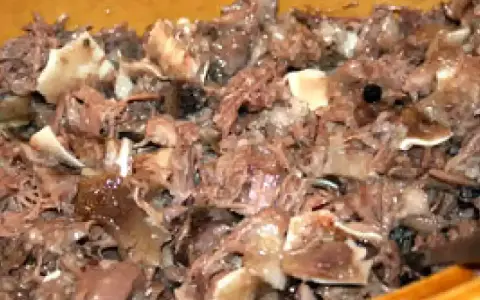 Un plat de fromage de tête, avec des morceaux de viande et de cartilage, dans un récipient en bois.