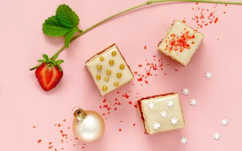 Délicieux petits fours sucrés, parfaits pour une recette de fête. Une fraise, une boule de Noël et des paillettes rouges complètent la scène.