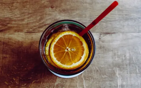 Verre de boisson sans alcool pour accompagner repas, avec rondelles d'orange et glaçons, sur fond de bois.