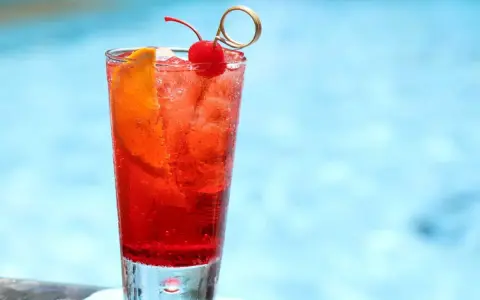 Un cocktail sans alcool à préparer la veille, garni d'une cerise et d'une tranche d'orange, prêt à être dégusté au bord de la piscine.