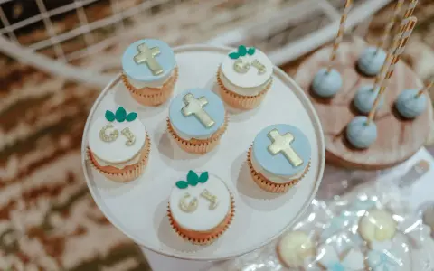 Jolis cupcakes décorés de croix dorées et de lettres pour un buffet dessert baptême. Des cake pops bleus sont aussi présents.