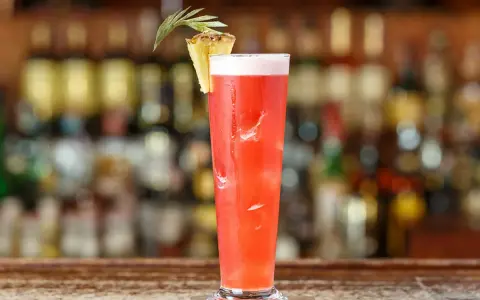 Un cocktail rouge vif, garni d'ananas, sur un bar. Idéal pour un cocktail pas cher pour 10 personnes, facile à préparer.