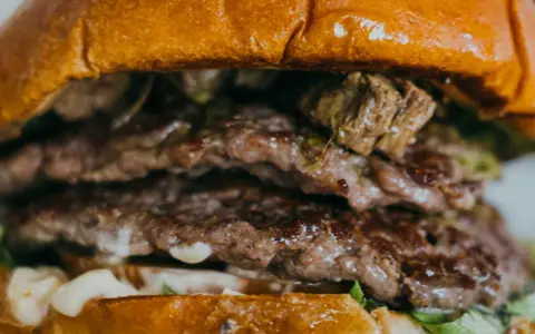Gros plan sur un steak burger double, avec des steaks juteux, de la sauce et de la laitue entre deux pains briochés dorés.