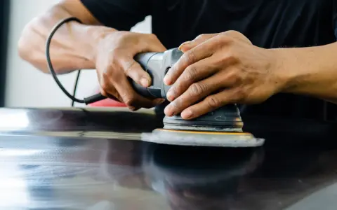 Mains polissant une surface sombre avec une ponceuse orbitale pour polir aluminium rayé.