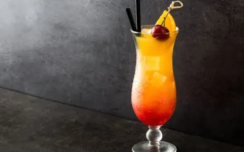 Cocktail Sex on the Beach recette 5l, dégradé rouge-orange, garni d'une cerise et d'une tranche d'orange.
