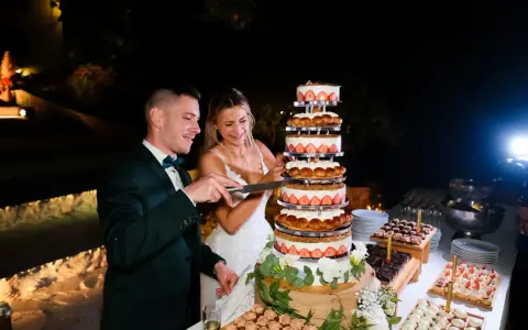 Un couple coupe un dessert mariage original, une tour de gâteaux aux fraises et à la crème, lors d'une réception nocturne.
