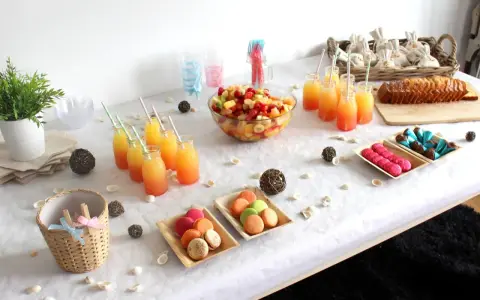 Buffet d'une idée gender reveal : jus de fruits colorés, salade de fruits, macarons roses et verts, gâteau, chocolats bleus et roses.