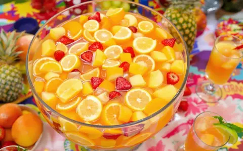 Un grand bol de punch aux fruits colorés, parfait pour une recette de punch sans alcool pour 30 personnes. Fraises, oranges, citrons et morceaux de pêche flottent dans un liquide orangé.