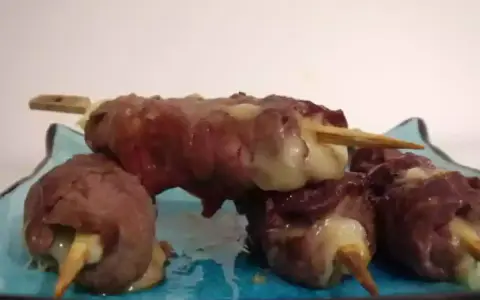 Brochettes de boeuf roulées autour de fromage fondant, servies sur une assiette bleue.