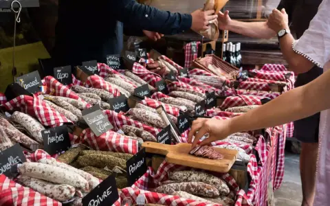 Vitrine de charcuterie avec de nombreuses saucisses et un client qui en choisit une tranche.