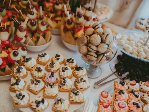 Délicieux assortiment de douceurs pour un brunch mariage : brochettes de fruits, mini gaufres à la crème, macarons et autres gourmandises.