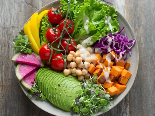 Un bol coloré avec avocat, tomates, pois chiches, patates douces, chou rouge, radis et poivron jaune. Parfaites salades originales pour buffet.