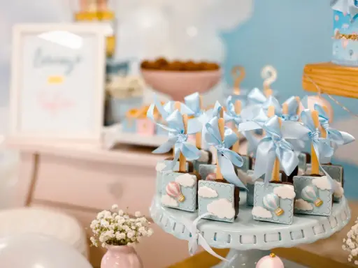 Garniture de table pour baby shower avec des chocolats décorés de montgolfières bleues et de nuages.