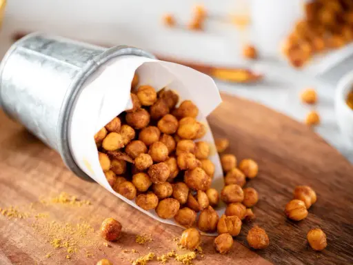 Un seau renversé déverse des pois chiches rôtis, parfaits pour des snacks sains. Une pincée d'épices dorées parsème le bois.