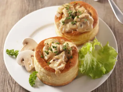 Deux bouchées à la reine maison, garnies d'une sauce crémeuse aux champignons et persil, servies avec des champignons frais et une feuille de laitue.