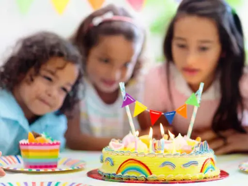 Trois enfants regardent un gâteau d'anniversaire jaune décoré d'arcs-en-ciel et de fanions. Le meilleur goût gâteau anniversaire est prêt à être dégusté.