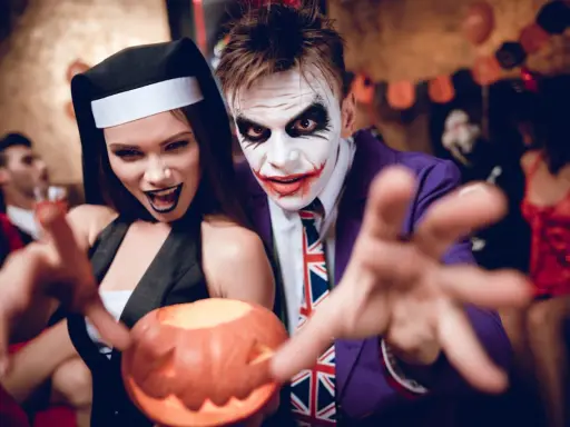Un couple en costumes effrayants, une nonne et le Joker, profite d'une **soirée costumée** d'Halloween, tenant une citrouille sculptée.